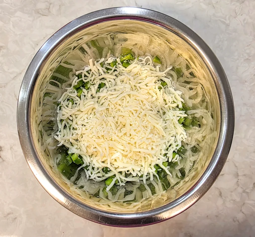 Grated mozzarella cheese added to the chopped capsicum in the bowl.