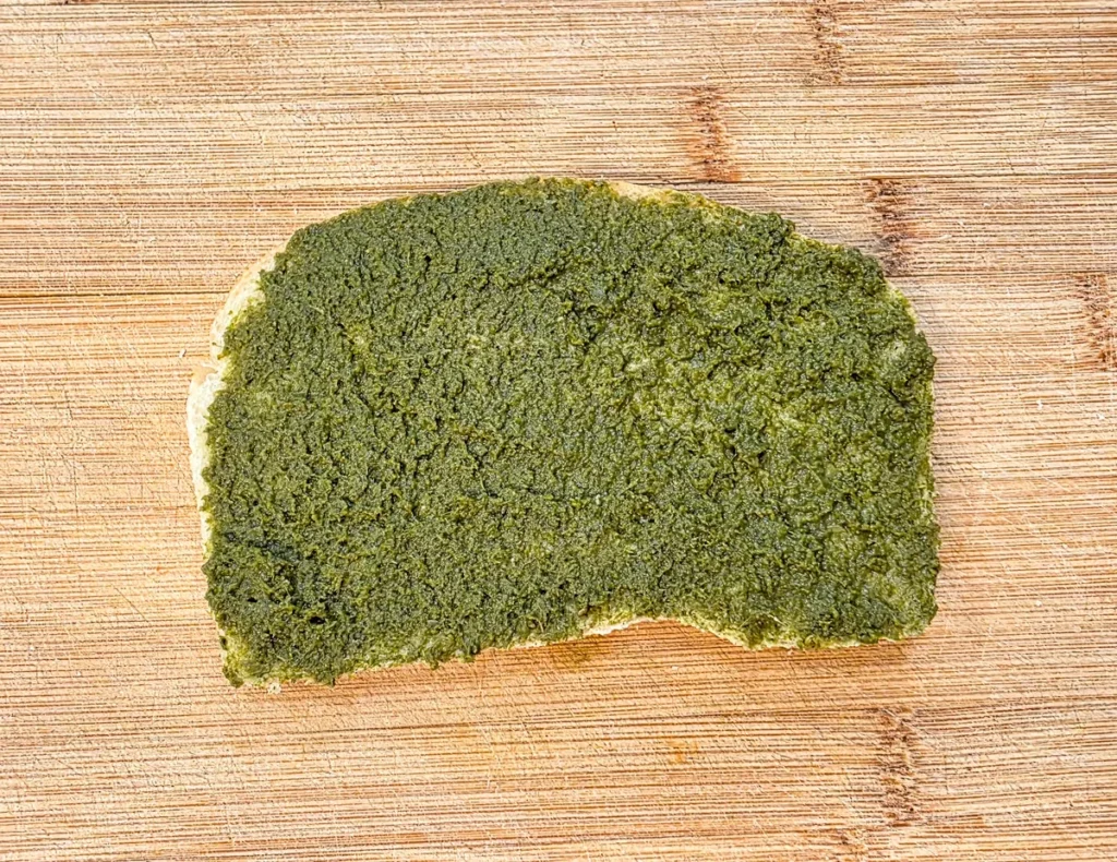 Green mint coriander chutney spread over a slice of sourdough bread.