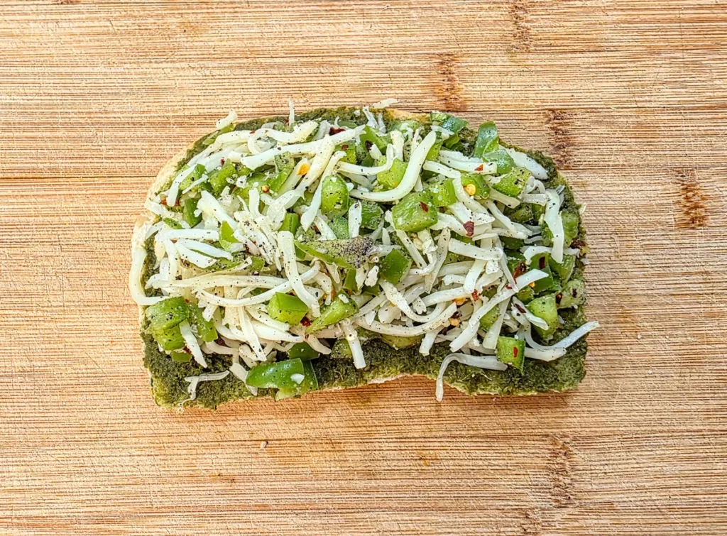 Cheese and capsicum filling spread evenly over the chutney layer on the bread.