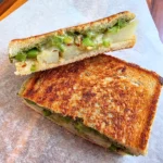 Grilled potato chutney sandwich cut in half, showing melted cheese, spiced potato slices and green chutney between toasted sourdough.